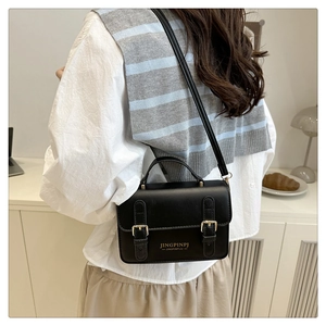 Detail view of the black leather small square bag with dual gold buckles and top handle