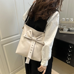 Chic beige shoulder bag featuring a large studded bow and elegant trapezoid shape