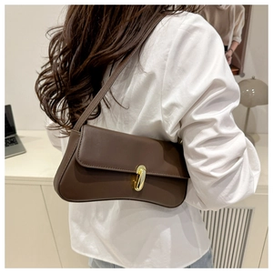 Close-up of a dark brown baguette bag with gold metal clasp worn by a model