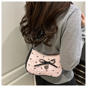 Close-up of pink crescent shoulder bag with black bows and a heart pendant