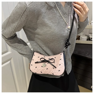 Fashionable pink crescent bag with black bow patterns shown on a model's shoulder
