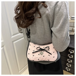 Detail of pink crescent bag with black bow embroidery and heart pendant on shoulder