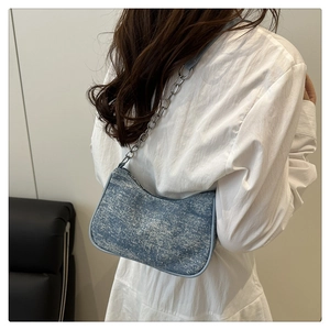 Détail du sac bandoulière en denim bleu avec chaîne argentée et finition vintage délavée