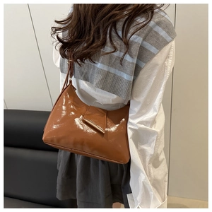 Brown glossy saddle bag with gold metal buckle shown as a crossbody shoulder style