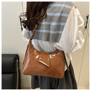 Brown patent leather saddle bag with gold triangle buckle shown on a female shoulder