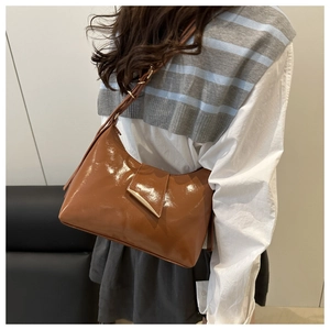 Detailed view of glossy brown patent leather shoulder bag with gold metal trim on model