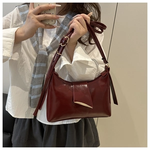 Détail du sac bandoulière en cuir brillant bordeaux avec boucle en métal doré porté