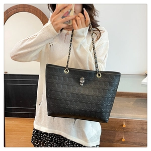 Close-up of black tote bag with skull embossing and silver metal skull charm pendant