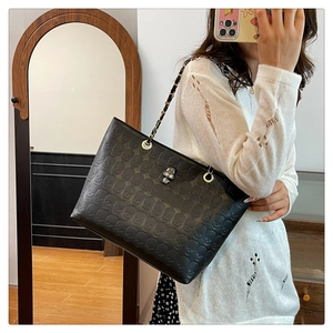 Close-up of black tote bag featuring skull embossed patterns and silver metal lock detail