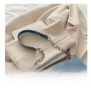Detail of blue denim shoulder bag featuring silver star emblem and chain strap on blazer
