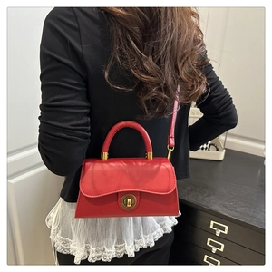 Red leather handbag with gold lock shown on model wearing black and white outfit