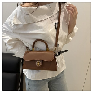Brown leather crossbody bag detail with circular metal turn-lock and vintage flap design