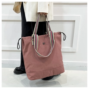 Detail of dusty rose tote bag featuring colorful striped handles and drawstring sides