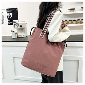 Detail of dark pink canvas tote bag with red blue white striped strap in a cafe