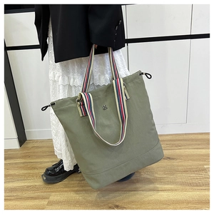 Detail of army green tote bag featuring colorful striped handles and a metal flower logo