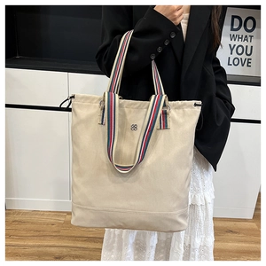 Close-up of beige canvas tote bag featuring striped straps and silver floral logo detail