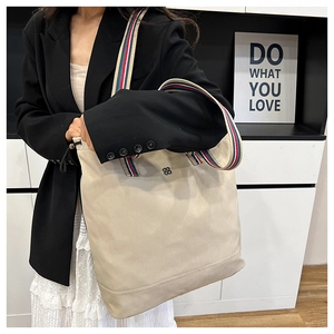 Detail of beige canvas tote bag with red and blue striped strap and metal flower logo