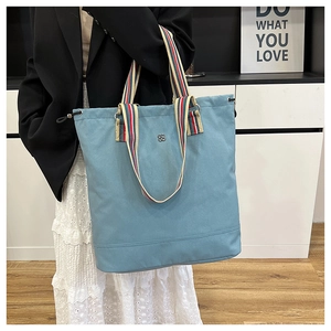 Light blue canvas tote bag featuring striped handles and small metal logo detail