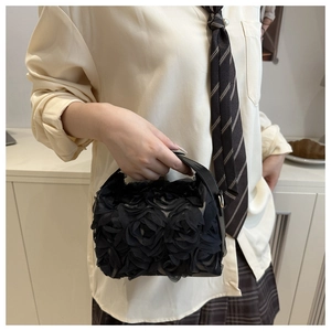 Détail d'un sac à main noir avec roses en tissu 3D et une poignée supérieure élégante