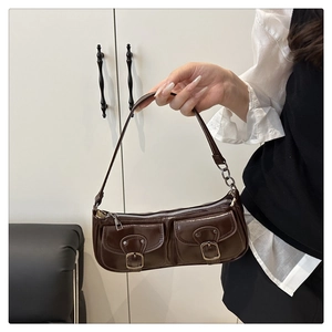 Detail of dark brown leather baguette bag with dual front pockets and silver buckle accents