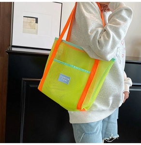 Detailed view of neon mesh beach tote bag with orange handles on model's shoulder