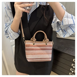 Detail of multi-color striped woven straw bucket bag with knots and leather crossbody strap