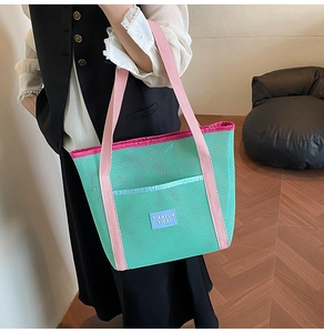 Detail of mint green mesh beach bag with pink handles and blue woven brand label