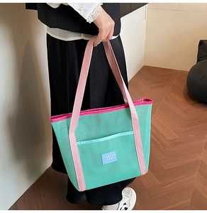 Detail of green mesh beach tote featuring pink handles and a convenient front pocket