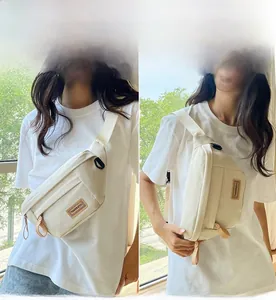 Close-up of minimalist cream canvas saddle bag featuring leather logo and adjustable strap