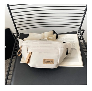 Detail of a minimalist cream-colored saddle bag showing the logo and nylon fabric texture