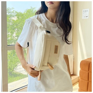 Detail of minimalist cream canvas crossbody bag showing logo and zipper pocket