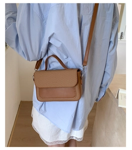 Brown patchwork crossbody bag with straw woven texture detail on a blue shirt