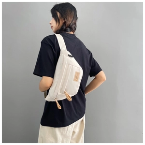 Detail view of cream canvas crossbody bag with leather zippers and brand logo on a model