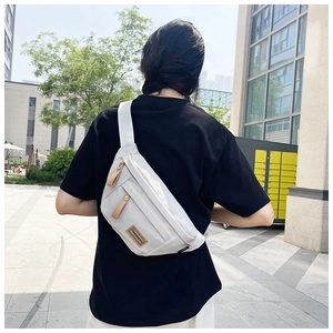 Outdoor lifestyle shot of a lightweight white nylon crossbody bag with dual brown zippers
