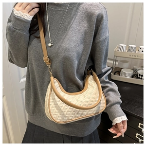 Detail view of woven beige half-moon underarm bag with brown leather trim and shoulder strap