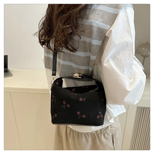 Detail of black canvas shoulder bag featuring red cherry prints and slim leather strap