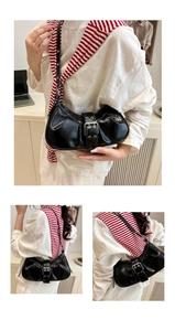 Detail view of black pleated underarm bag with decorative silver buckle and glossy finish