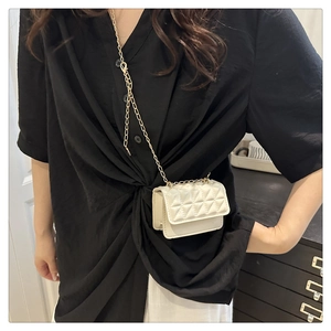 Detail of cream quilted mini crossbody bag with gold chain strap on black shirt