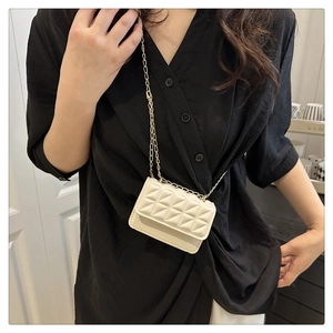 Detail of white quilted mini crossbody bag with golden chain strap on black dress
