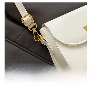 Detail of gold metal buckle and hardware on white leather crossbody handbag strap