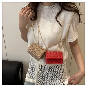 Close-up of beige and red quilted mini chain bags worn with a white knit vest