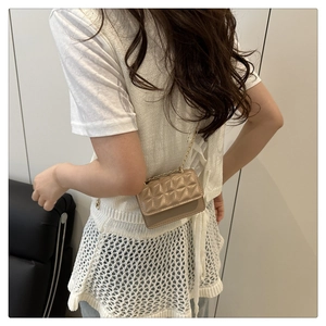Detailed view of beige quilted crossbody bag with gold chain strap worn by a model