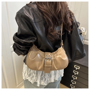 Detail view of beige ruched half-moon bag with decorative silver buckle on glossy leather
