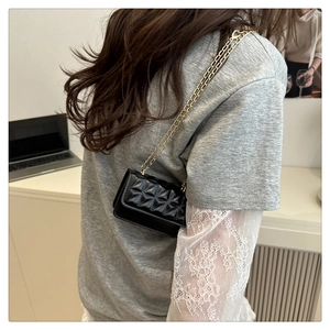 Detail of a black quilted mini crossbody bag with a gold chain strap worn by a model