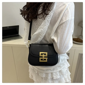 Detail of a minimalist black crossbody bag featuring a large gold geometric buckle