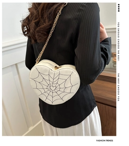 White heart-shaped crossbody bag featuring black spider web embroidery and gold chain