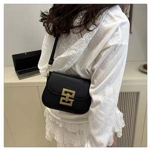 Detail of minimalist black crossbody bag with geometric gold clasp worn by a model