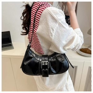 Detail of a black glossy crescent shoulder bag with silver buckle and grommet accents