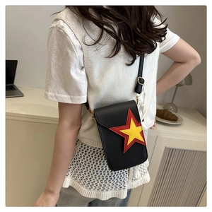 Détail d'un petit sac bandoulière noir avec patchs étoiles rouges et jaunes sur un bureau