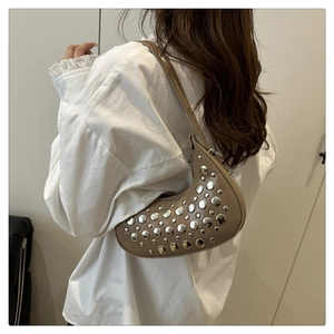 Close-up of beige crescent bag with silver rivets worn over the shoulder by a model